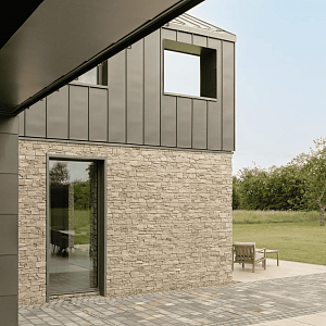 Дом с фасадом, облицованным натуральным камнем RKS SLATE Кварцит Sesame Yellow Country, в солнечном свете. Видно общее впечатление от облицовки и гармонию с окружающей средой.