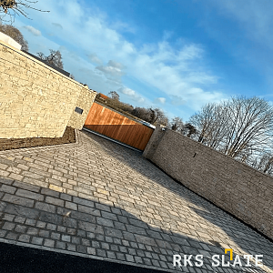 Забор, облицованный натуральным камнем RKS SLATE Кварцит Sesame Yellow Country в солнечном свете. Камень создает привлекательный внешний вид и гармонирует с окружающим ландшафтом.